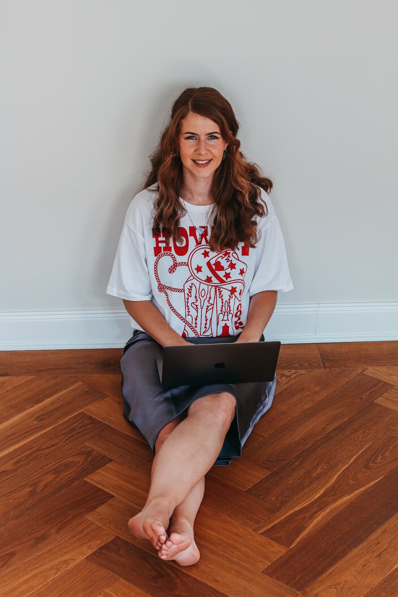 Carina Michels sitzt lächelnd auf dem Boden und hat einen Laptop auf dem Schoß